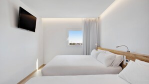 Una habitación de hotel moderna con dos camas, un televisor de pantalla plana montado en la pared, una ventana con cortinas y un cabecero de madera.