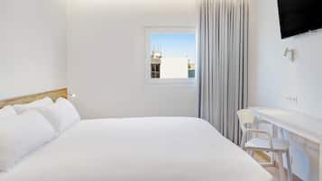 Quarto de hotel moderno com uma cama grande, uma escrivaninha com cadeira, televisão presa na parede e janela com vista para edifícios.