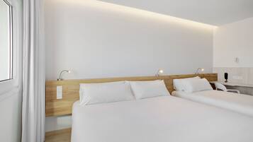 Habitación de hotel con dos camas, cabecero de madera, lámparas de noche, pared blanca y ventana con cortinas.