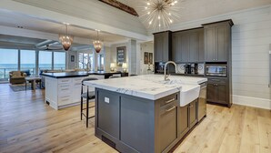 A modern kitchen with a large island, dark cabinetry, and a view to the ocean. - 95 Dune Lane -Oceanfront | Island Oasis | Booking now for 2027! (Hilton Head Island)