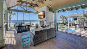 A covered outdoor area with a stone fireplace, seating, and a view of the ocean. - 95 Dune Lane -Oceanfront | Island Oasis | Booking now for 2027! (Hilton Head Island)