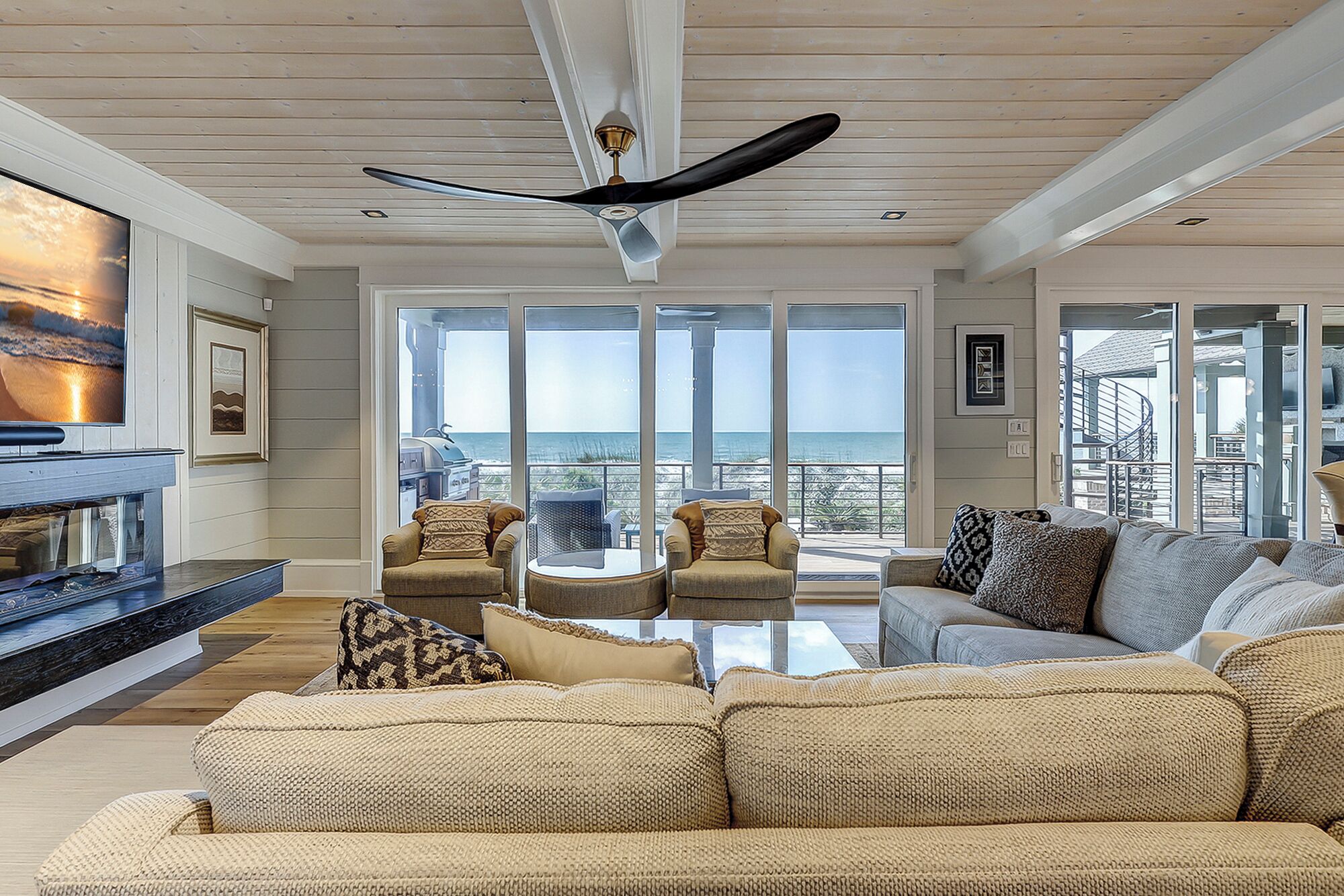 A spacious living room with a large window overlooking the ocean, a ceiling fan, and a fireplace.
