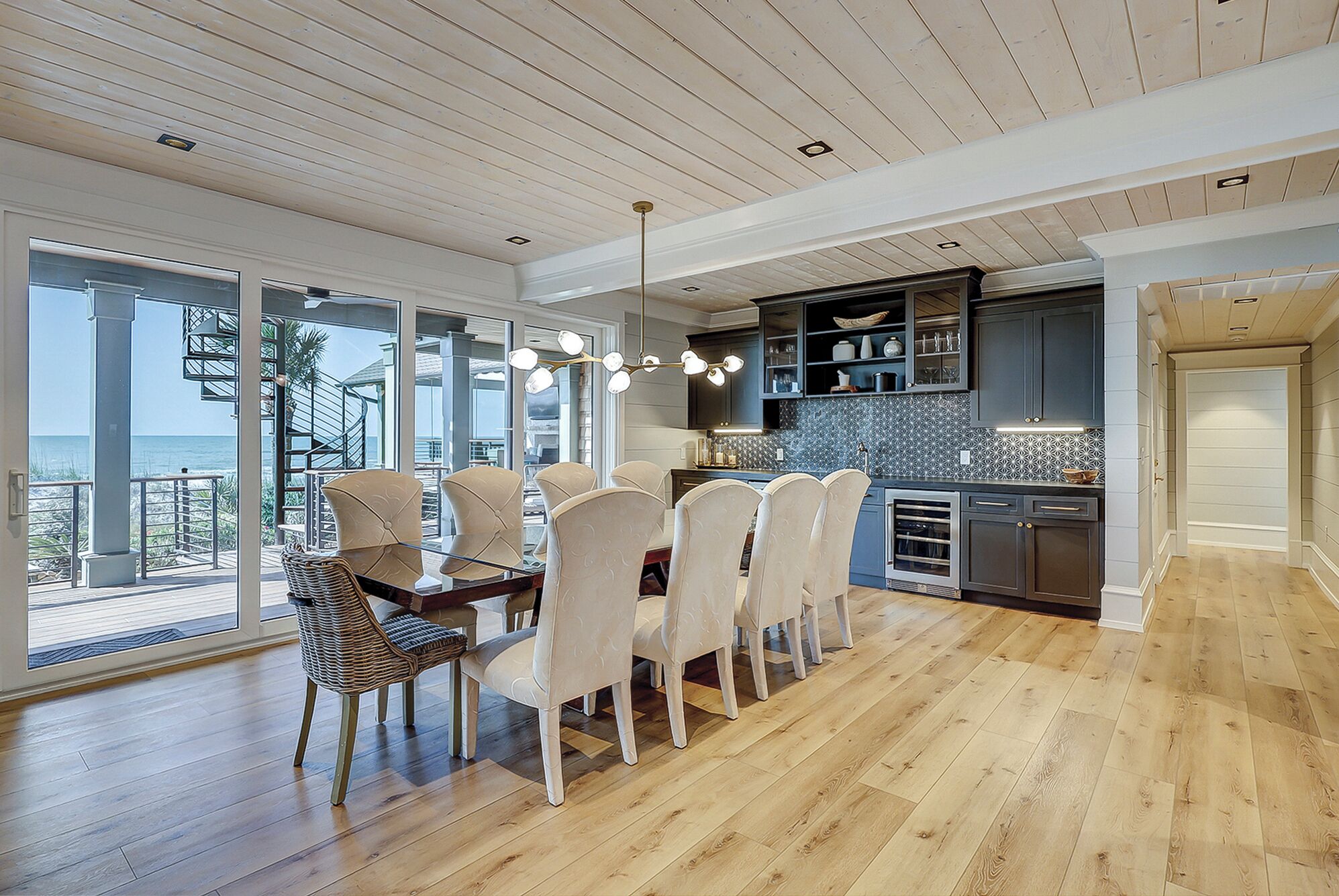 Une salle à manger spacieuse avec vue sur l’océan, un plancher en bois et des meubles de cuisine modernes.