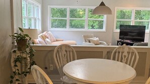 En matplats med ett runt bord och fyra stolar, en krukväxt och ett fönster med utsikt över grönområden.