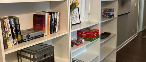 Un couloir avec des étagères blanches, dont certaines contiennent des livres, un pot rempli de crayons et un vase avec des fleurs.
