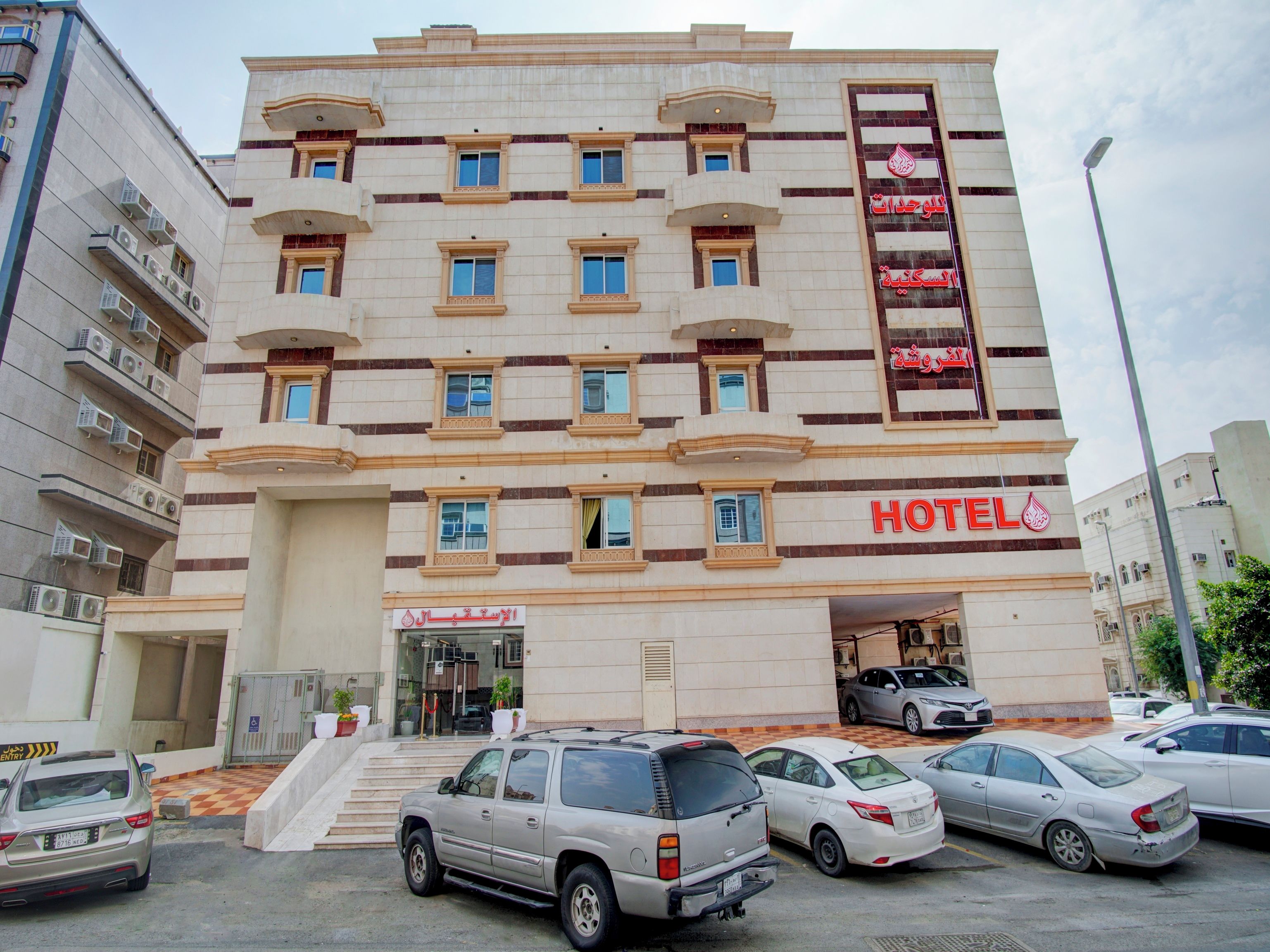 Un hotel de varios pisos con un llamativo letrero 'HOTEL', una entrada con portones y varios coches aparcados en la parte delantera.