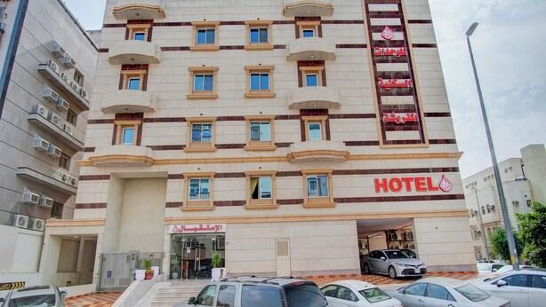 Un hotel de varios pisos con un letrero grande que dice 'HOTEL', una entrada con portones y varios coches aparcados.