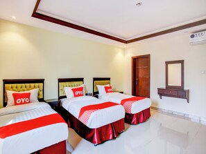 A hotel room with three beds, each with a red and white bedspread and pillows with 'OYO' branding. There is a wooden dresser with a mirror and a wall-mounted air conditioning unit. - Al Tamayoz Al Raqi Al Salamah (Jeddah)