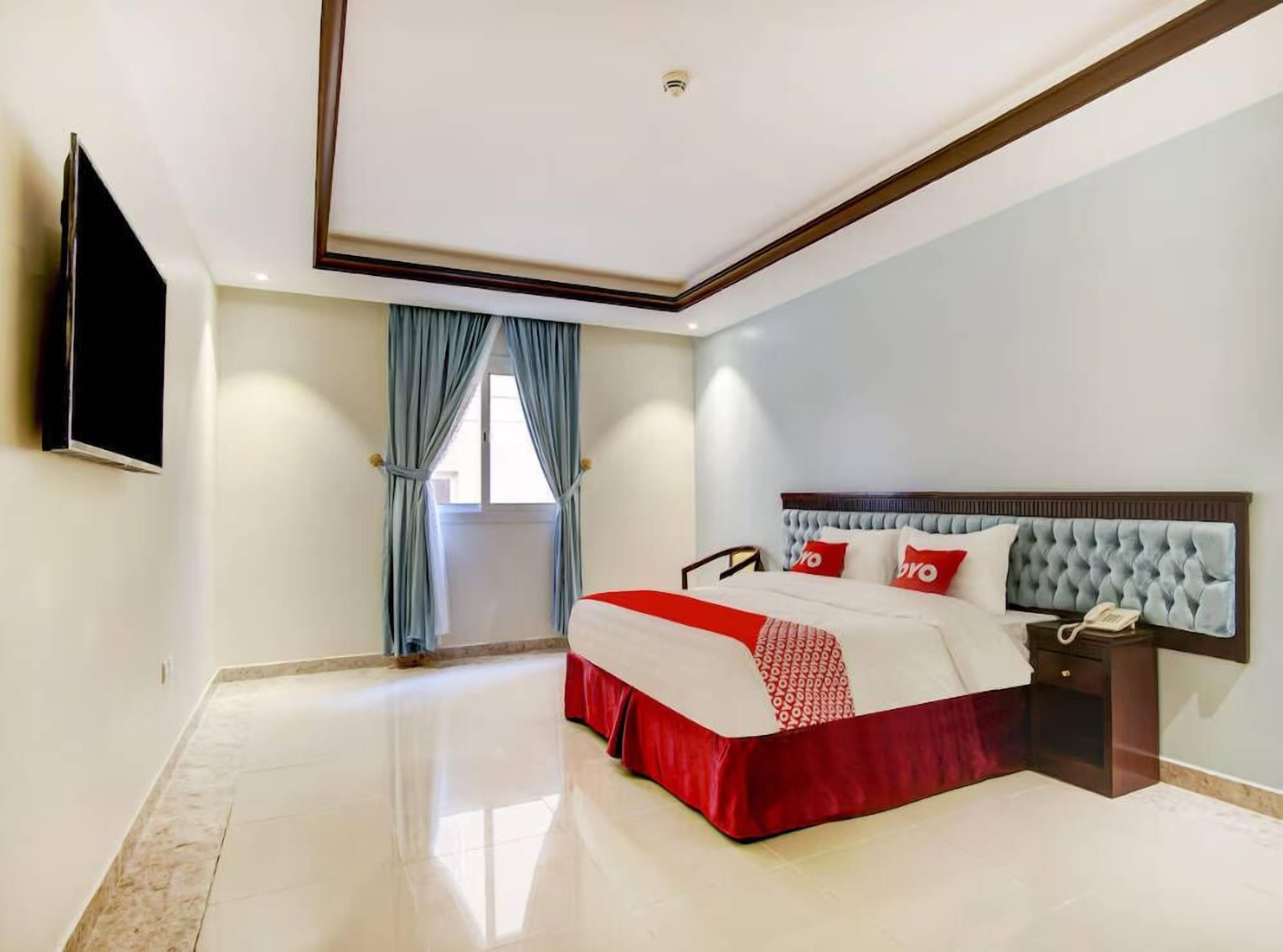Habitación de hotel con una cama grande, una mesita de noche con teléfono y un televisor de pantalla plana montado en la pared.