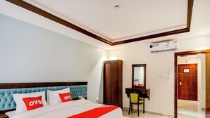 Habitación de hotel con una cama grande, un armario de madera, un escritorio con una silla, un espejo y una puerta que da a otra habitación.