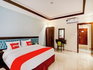 A hotel room with a large bed, a wooden wardrobe, a desk with a chair, a mirror, and a door leading to another room. - Al Tamayoz Al Raqi Al Salamah (Jeddah)