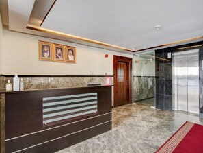 A reception desk with framed portraits, a wooden door, a glass elevator, and a marble floor. - Al Tamayoz Al Raqi Al Salamah (Jeddah)