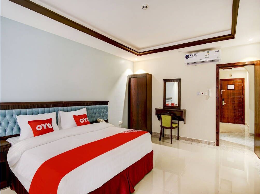 Habitación de hotel con cama, escritorio, silla, espejo y unidad de aire acondicionado.