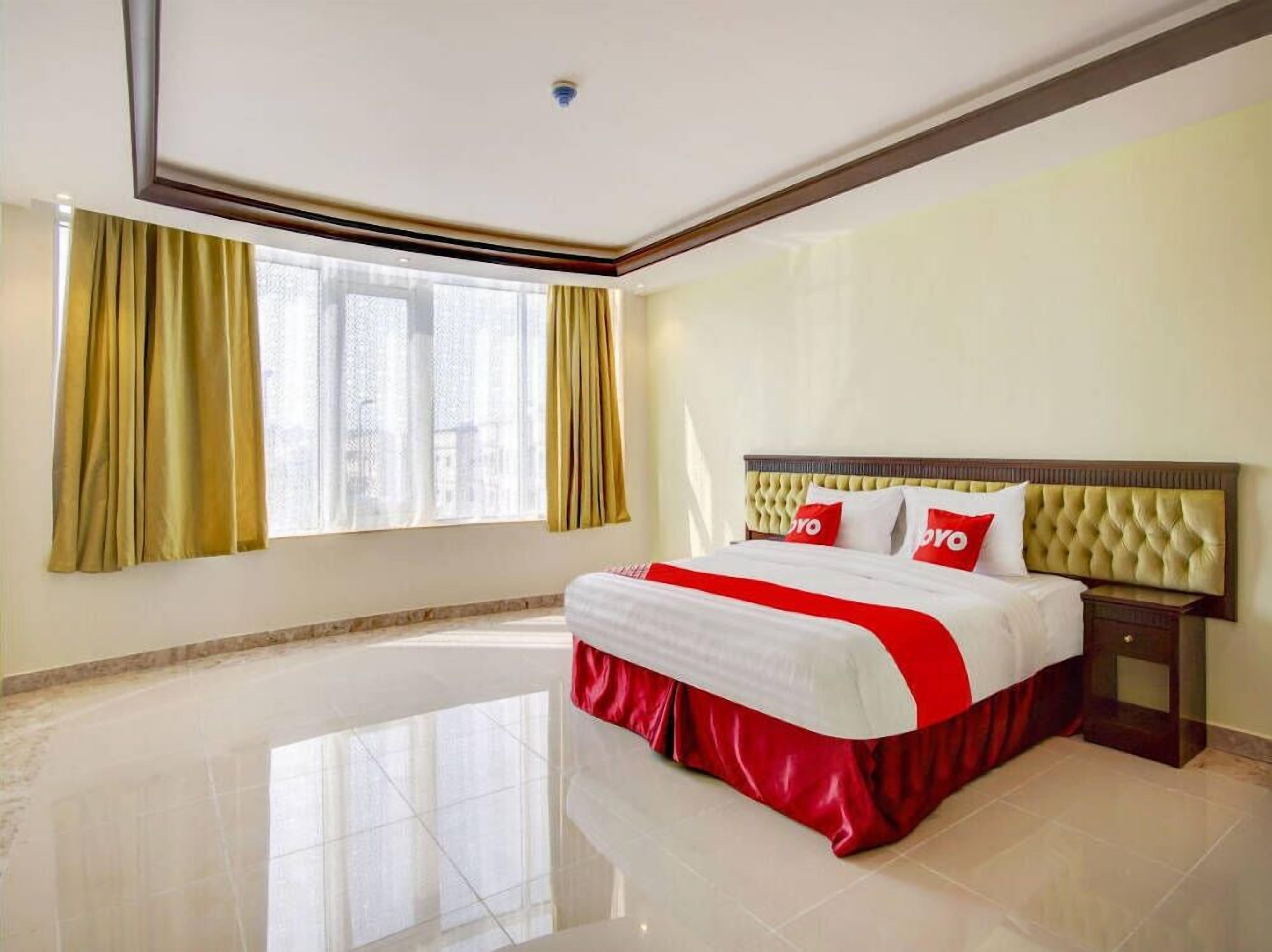 Una habitación de hotel con una cama grande, una mesita de noche, una ventana con cortinas y una lámpara en el techo.