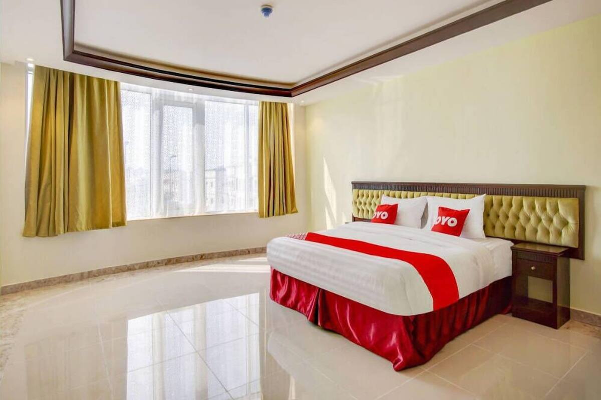 Une chambre d’hôtel avec un grand lit, une table de chevet, une fenêtre avec des rideaux et un luminaire au plafond.