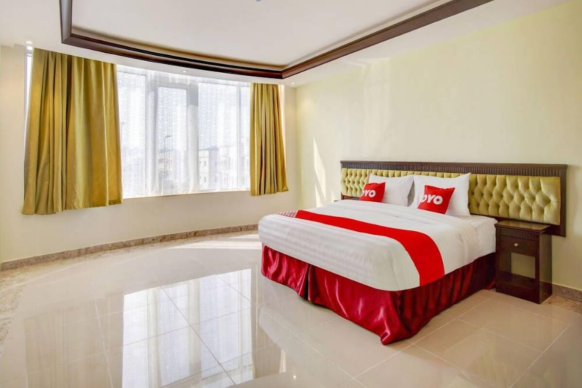 Una habitación de hotel con una cama grande, una mesita de noche, una ventana con cortinas y una lámpara en el techo.