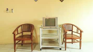 A room with two wooden chairs, a television on a stand, and a wall with two framed items.