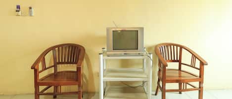 A room with two wooden chairs, a television on a stand, and a wall with two framed items.