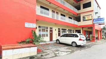 Um edifício de vários andares com fachada vermelha e bege, um carro branco estacionado na frente e um aviso indicando 100% de ocupação.