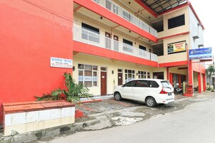A multi-story building with a red and beige facade, a white car parked in front, and a sign indicating a 100% occupancy rate.