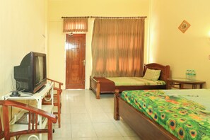 Una habitación de hotel con una cama, una silla de madera, una mesita, un televisor y una puerta.