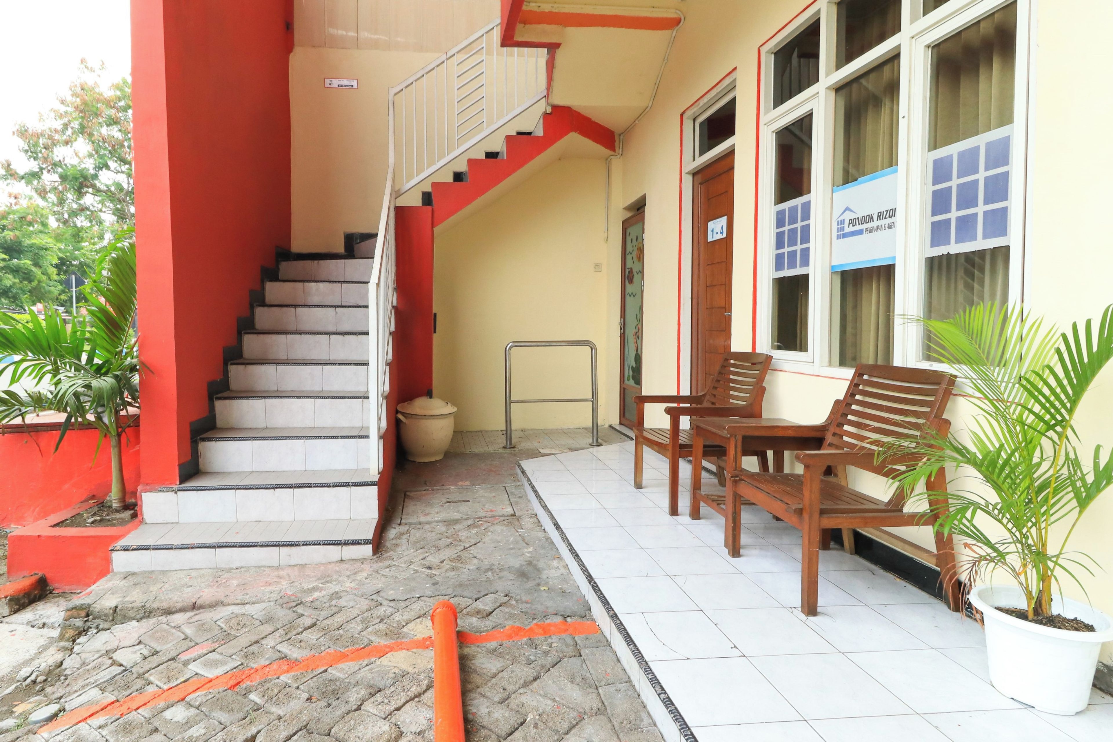 A building with a staircase, a wooden bench, and potted plants.