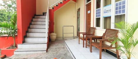 A building with a red exterior, a staircase leading to an upper floor, a bench, and potted plants.
