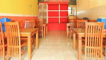 Interior de restaurante com mesas e cadeiras de madeira, piso de azulejos e balcão vermelho.