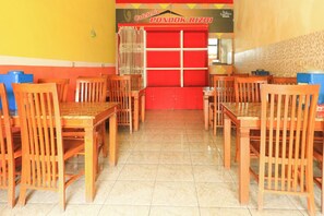 Interior de restaurante com mesas e cadeiras de madeira, piso de azulejos e balcão vermelho.