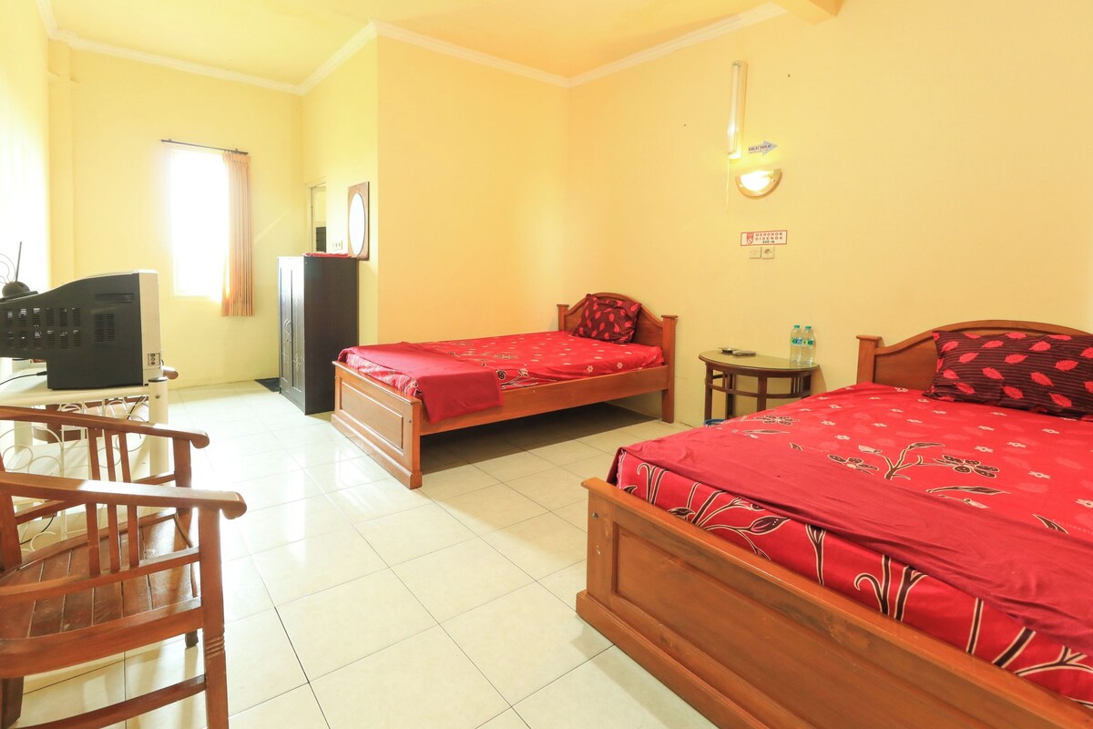 Quarto com duas camas de madeira, uma cadeira de madeira, uma televisão e uma mesa pequena com uma garrafa.