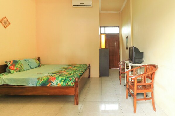 Quarto com cama, escrivaninha com cadeira, ar condicionado e porta para outro cômodo.