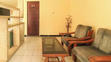A room with a wooden door marked '2nd 7th', a glass-top table, two wooden armchairs, and a small potted plant.