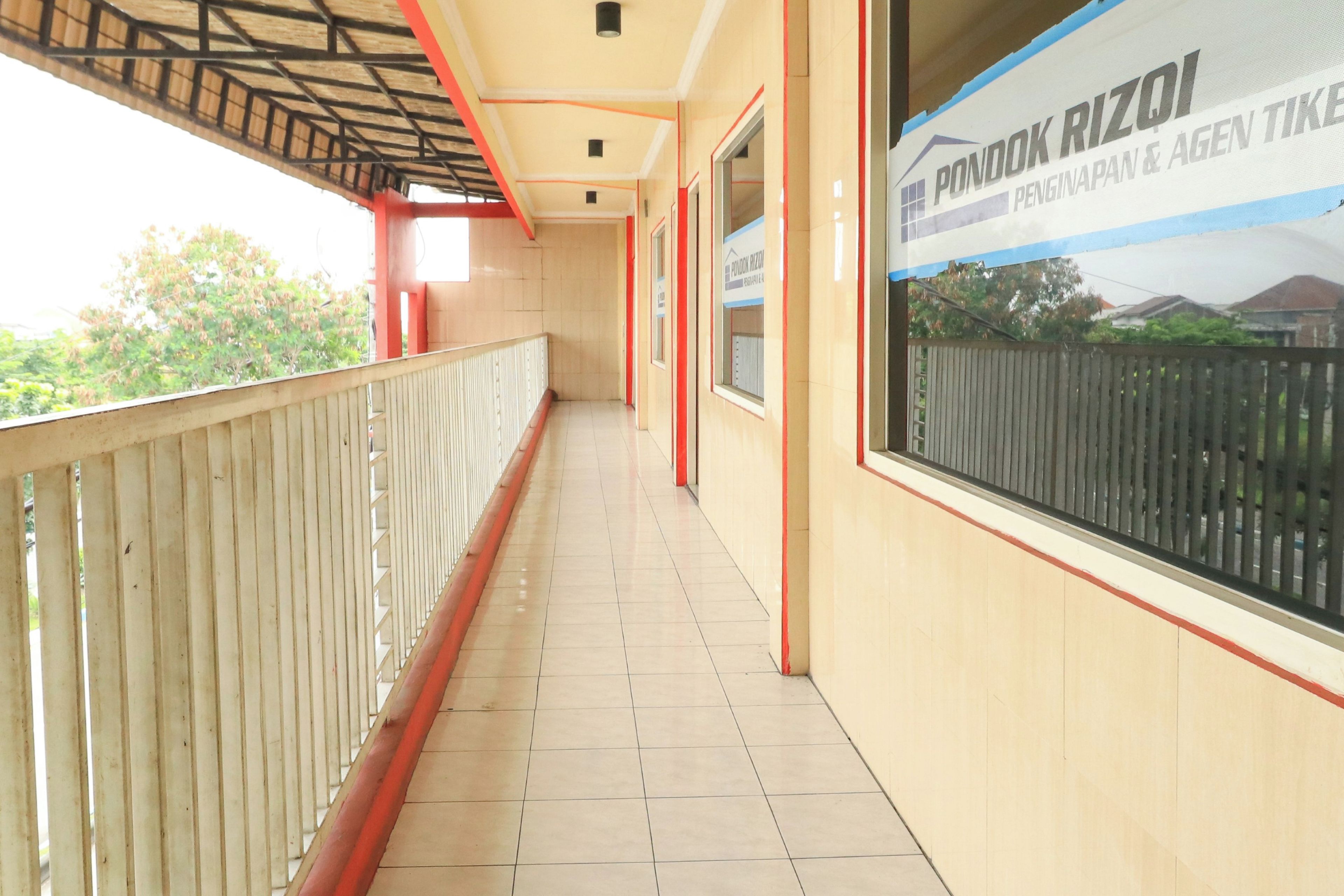 A corridor with a tiled floor, a railing on one side, and a large window on the opposite wall.