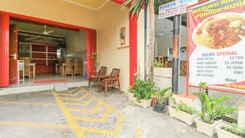 A restaurant entrance with a red door, outdoor seating, and a menu board advertising special dishes.