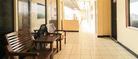 A hallway with wooden benches, a tiled floor, and a door with a number sign.