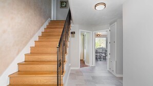 Eine Holztreppe mit schwarzer Geländer führt zu einem Raum mit Fliesenboden und einer Tür zum Essbereich.