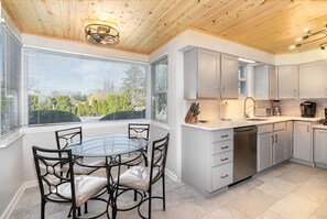 A modern kitchen with white cabinets, a dishwasher, and a dining area with a glass table and metal chairs. - IN-GROUND POOL, Large Private Fenced Yard, Dining Gazebo, Outdoor Kitchen/Bath (Mechanicsburg)