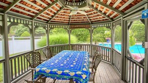 Eine überdachte Terrasse mit Tisch und Stühlen, einem Deckenventilator und Blick auf einen Swimmingpool.