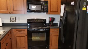 Uma cozinha com armários de madeira, geladeira preta, micro-ondas, forno e cafeteira.