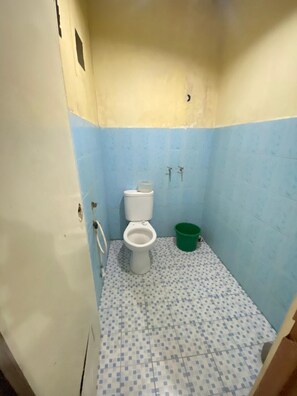 Un baño pequeño con inodoro, un cubo verde y un suelo con estampado azul y blanco.