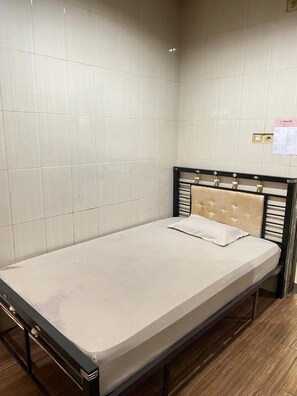 Una cama individual con cabecera, suelo de madera y paredes de azulejos.