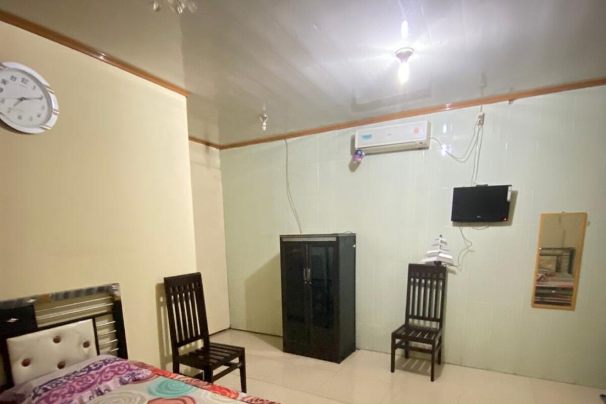 Un dormitorio con cama, dos sillas, un armario, una televisión y un reloj en la pared.
