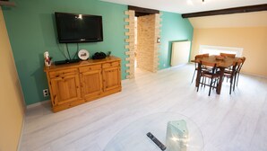 A dining area with a wooden table and chairs, a television mounted on the wall, and a brick wall feature. - Burgundian loft at the foot of the Seine springs (Chanceaux)