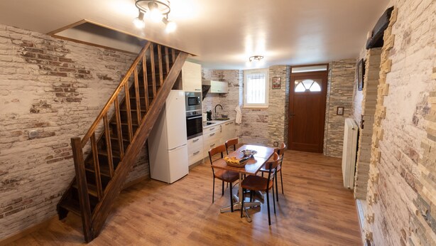 A kitchen with a wooden staircase, a dining table with chairs, and a stone wall. - Burgundian loft at the foot of the Seine springs (Chanceaux)