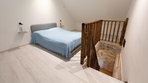 A bedroom with a bed, a wooden staircase, and a white wall. - Burgundian loft at the foot of the Seine springs (Chanceaux)