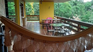 Eine Hängematte unter einer Holzbalkendecke mit Blick auf eine Terrasse, inklusive Tisch und Stühlen, und einer gelben Wand.