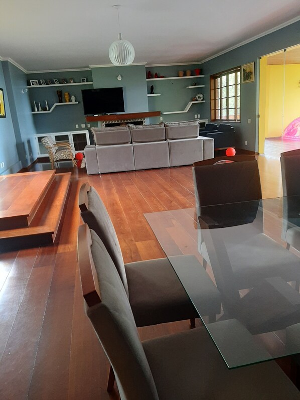 A modern living room with a glass dining table, grey sofa, and wooden flooring.