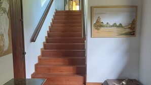 Eine Holztreppe führt zu einer zweiten Etage, ein Gemälde an der Wand und ein kleiner Tisch mit einem dekorativen Gegenstand.