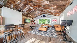 A spacious living area with a high ceiling, a large window, a TV, a bike, and a bar area with stools. - Your Perfect Southwest Michigan Lakehouse Getaway (Paw Paw)