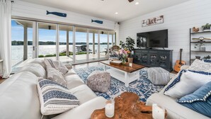 A spacious living room with a large window overlooking a lake, a ceiling fan, and a flat-screen TV. - Your Perfect Southwest Michigan Lakehouse Getaway (Paw Paw)